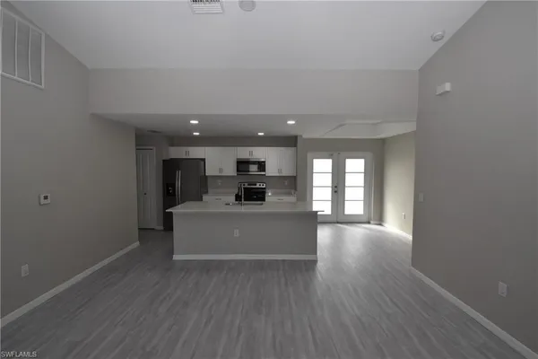 a view of a kitchen and an empty room with wooden floor and a window