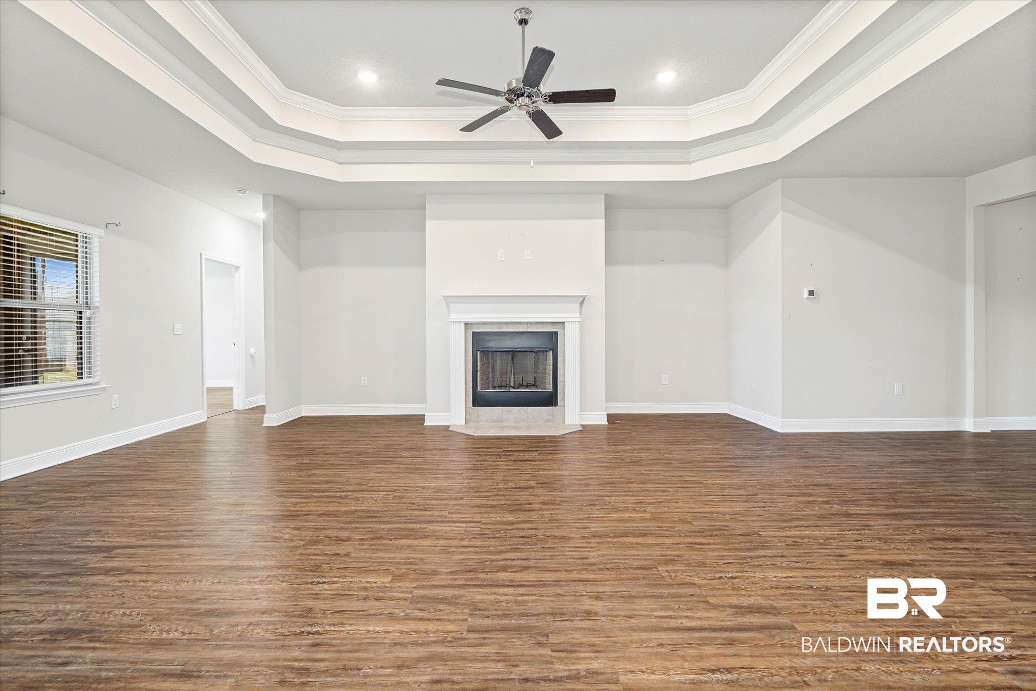 10207 Dunleith Loop Daphne, AL 36526 - Photo 3 of 23 Unfurnished living room with ornamental molding, dark wood-style flooring, a fireplace, a raised ceiling, and ceiling fan