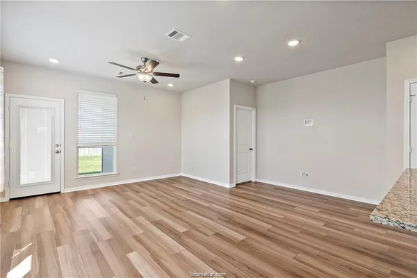 a view of an empty room with wooden floor and a ceiling fan