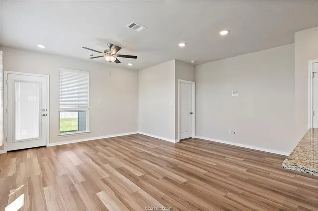 a view of an empty room with wooden floor and a ceiling fan