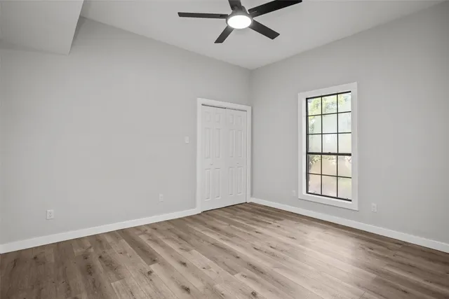 an empty room with wooden floor fan and windows