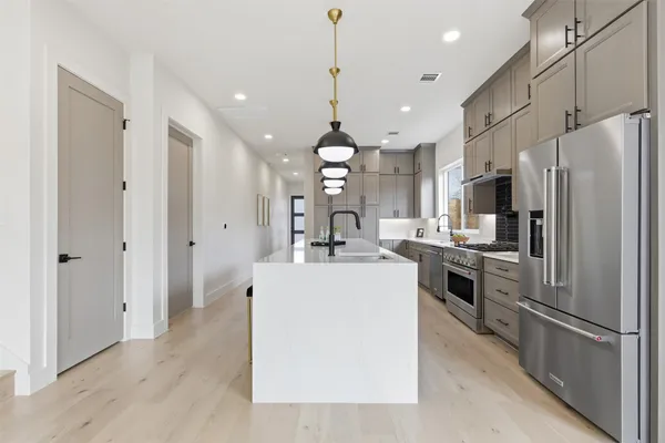 a kitchen with stainless steel appliances kitchen island granite countertop a refrigerator oven a sink dishwasher and a refrigerator with wooden floor