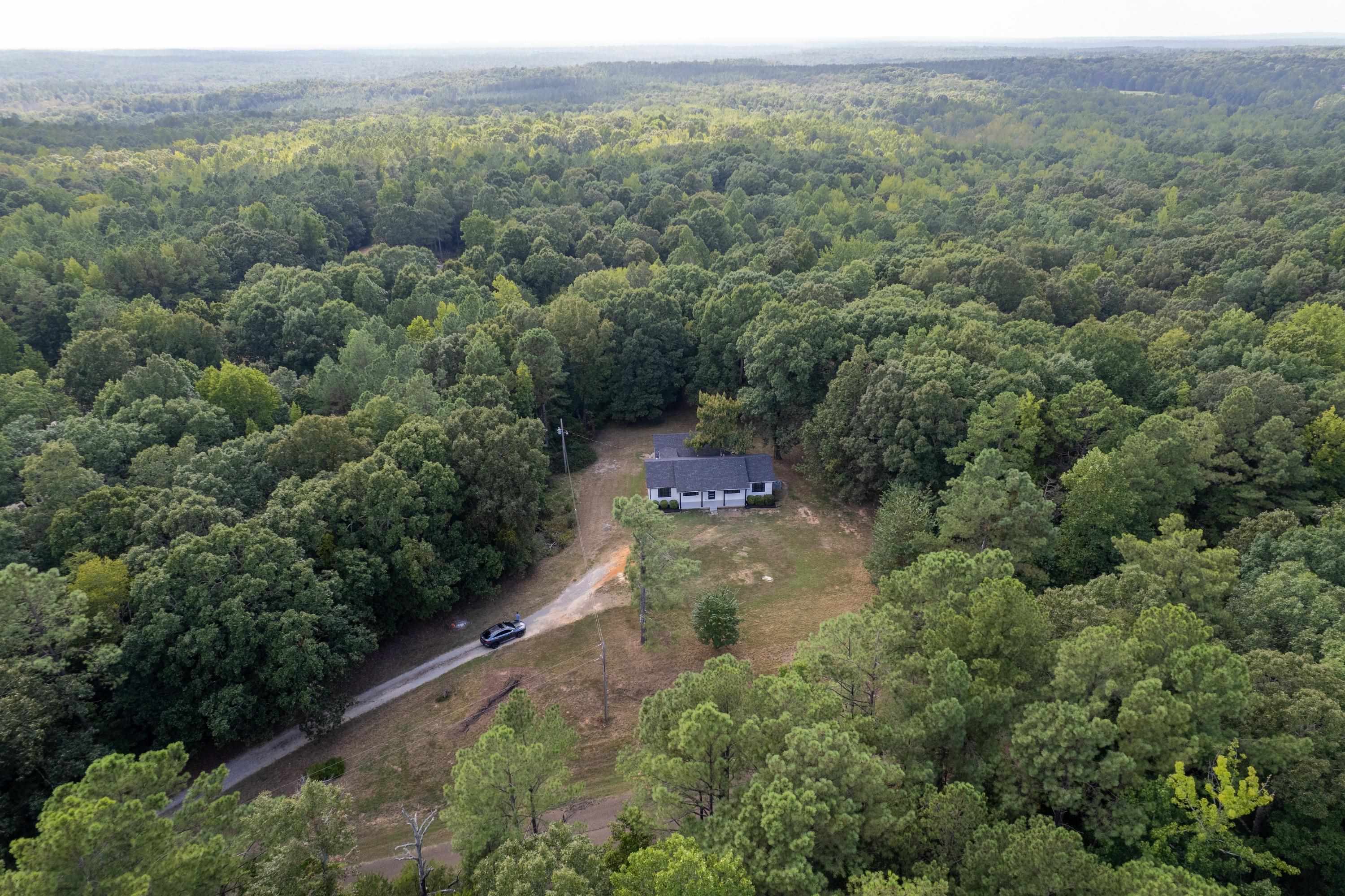 3690 Callahan Road Middleton, TN 38052 - Photo 7 of 26 Single-story property with a light-colored exterior and dark roof situated amidst extensive tree coverage