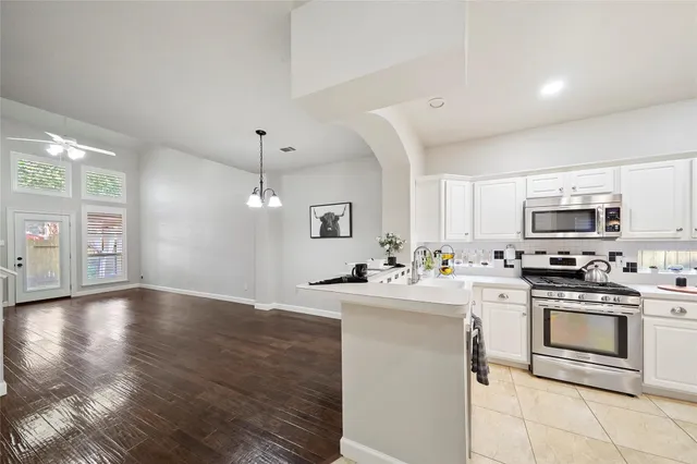 a kitchen with stainless steel appliances a stove top oven a sink a refrigerator white cabinets and wooden floor