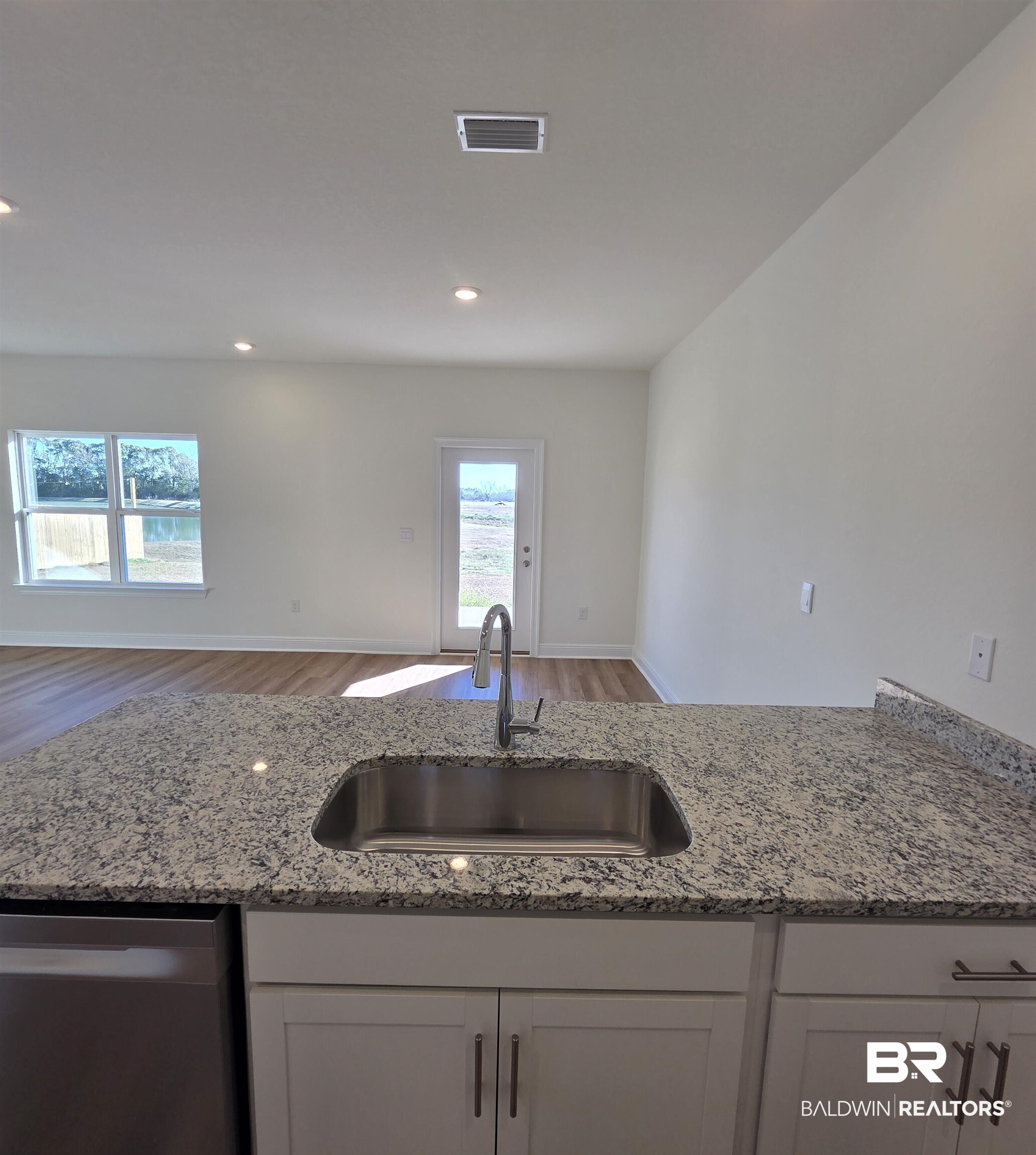 28084 Hallow Trail Elberta, AL 36530 - Photo 18 of 21 Kitchen with stainless steel dishwasher, light stone counters, white cabinets, open floor plan, and wood finished floors