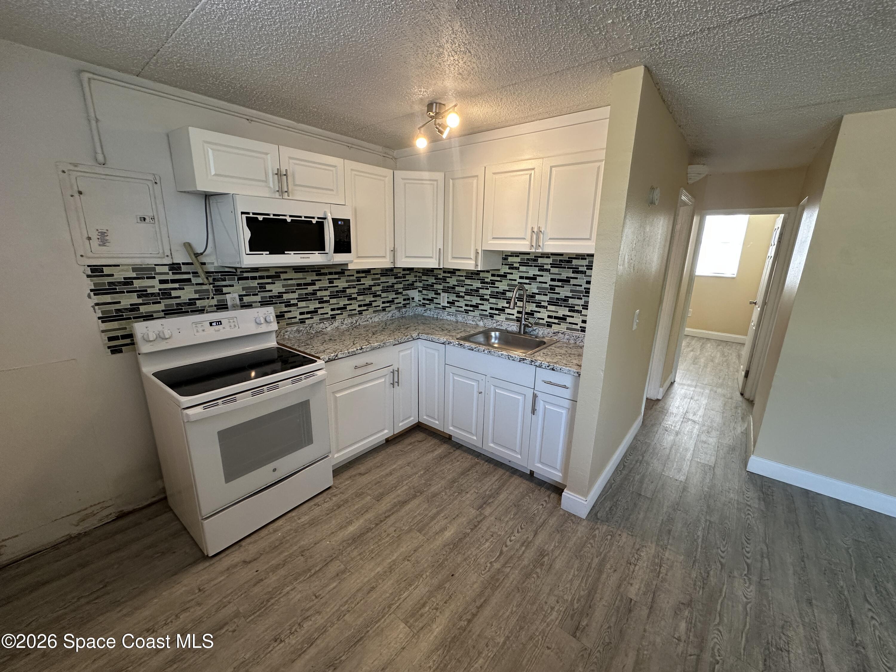 240 Stone Street, Unit 6 Cocoa, FL 32922 - Photo 4 of 7 a kitchen with stainless steel appliances white cabinets and wooden floor