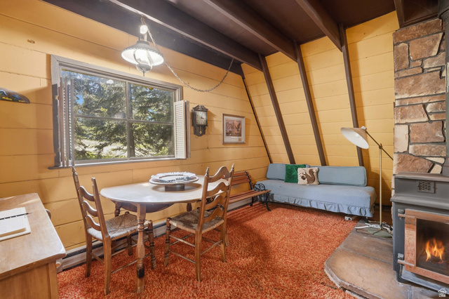 8505 South Snake Crk Road Salt Lake City, UT 84121 - Photo 12 of 67 Living area featuring a stone-clad fireplace with an attached wood-burning stove, sloped wood-paneled walls, and exposed ceiling beams