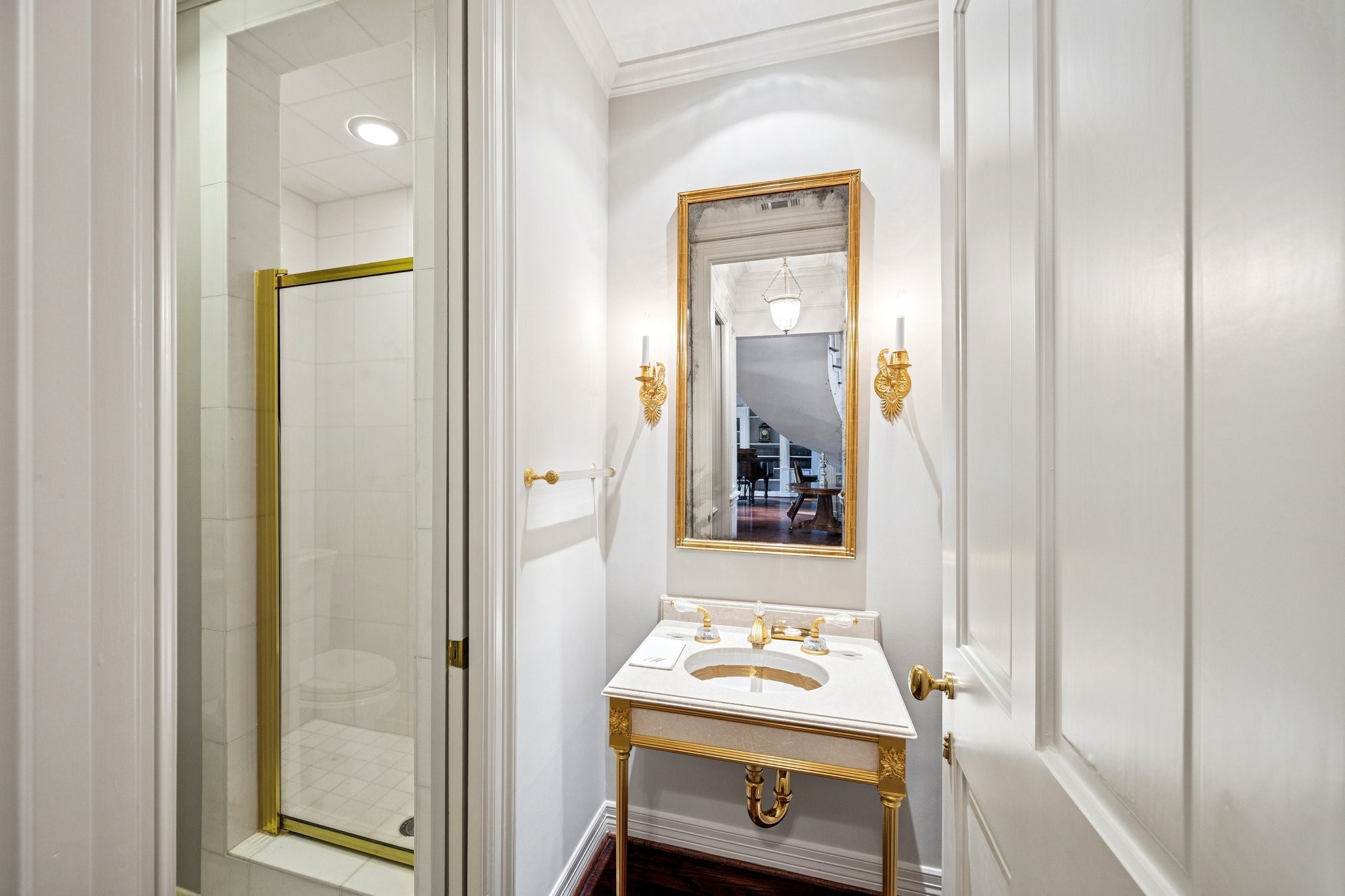 2249 Pelham Drive Houston, TX 77019 - Photo 15 of 50 An exquisite jewel-box bath featuring a sculptural console vanity, elegant gold fixtures, and a glass-enclosed shower, all framed by classic millwork and soft designer lighting.