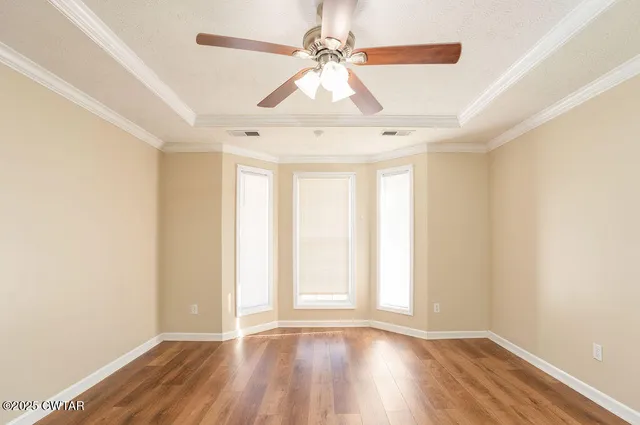 an empty room with wooden floor fan and windows
