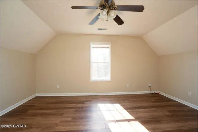 an empty room with wooden floor ceiling fan and windows