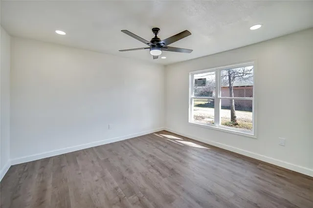 an empty room with wooden floor fan and windows