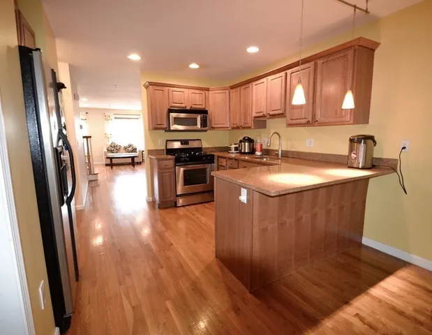 a kitchen with stainless steel appliances granite countertop a refrigerator a sink dishwasher a stove top oven a refrigerator with wooden floor and cabinets