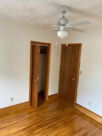 a view of an empty room with wooden floor and a ceiling fan