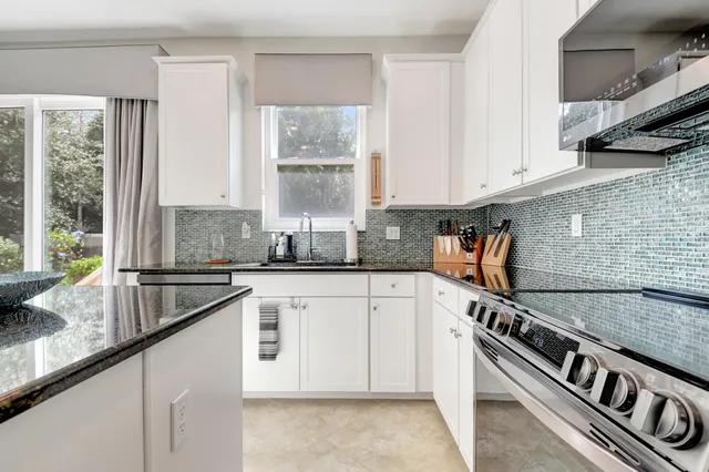 a kitchen with granite countertop a sink stainless steel appliances white cabinets and a window