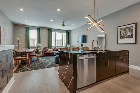 a living room with stainless steel appliances granite countertop a couch a sink dishwasher a living room with couches and potted plants with wooden floor