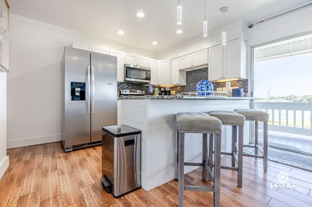a kitchen with stainless steel appliances granite countertop a refrigerator a stove top oven a sink dishwasher and white cabinets with wooden floor