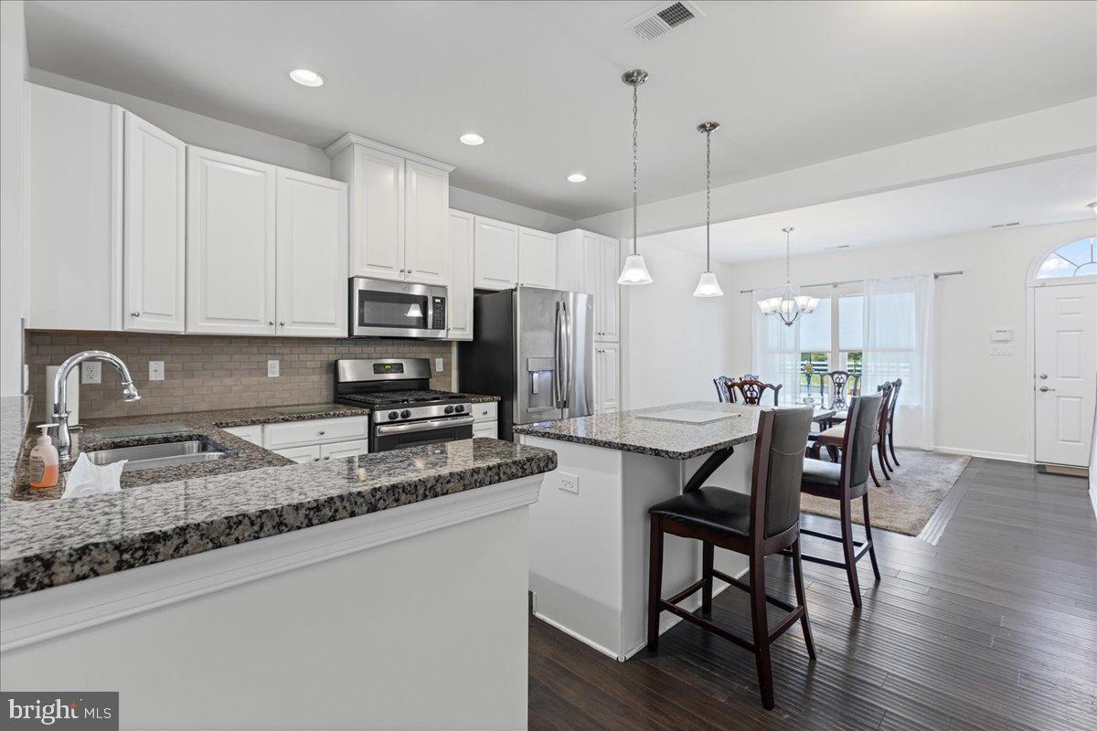54 Heals Farm Road Burlington, NJ 08016 - Photo 7 of 26 a kitchen with stainless steel appliances granite countertop a stove a sink a microwave a dining table and chairs with wooden floor