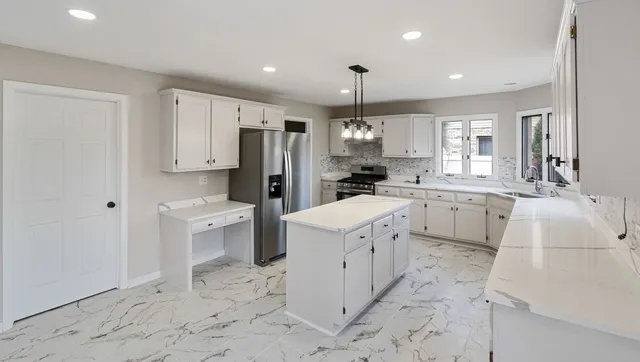 a large white kitchen with a stove a sink dishwasher a refrigerator and white cabinets with wooden floor