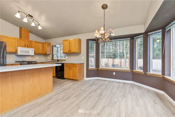 a open kitchen with granite countertop a stove top oven a sink dishwasher a dining table and chairs with wooden floor