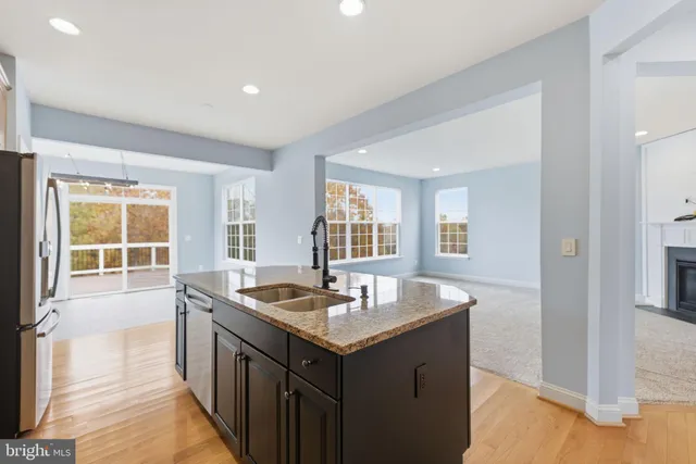 a view of kitchen with stainless steel appliances granite countertop a stove a refrigerator a sink a dining table and chairs with wooden floor