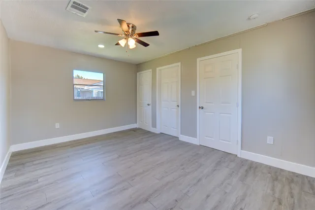 an empty room with wooden floor ceiling fan and window