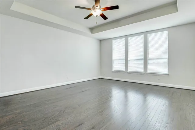 an empty room with wooden floor chandelier fan and windows