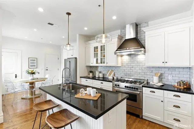 a kitchen with stainless steel appliances granite countertop a stove a sink a refrigerator and white cabinets with wooden floor