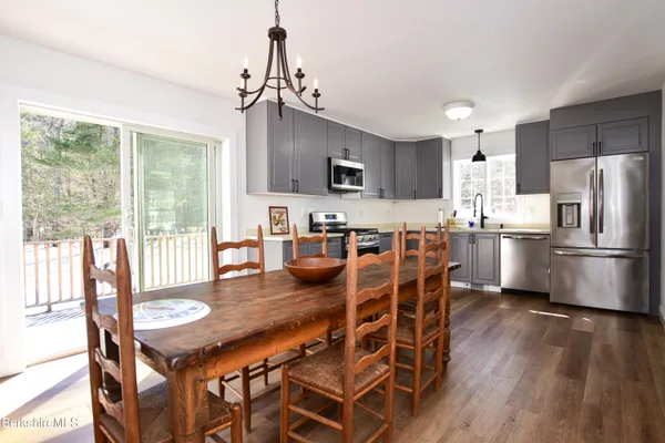 a kitchen with stainless steel appliances granite countertop a stove a refrigerator a microwave oven a dining table and chairs with wooden floor