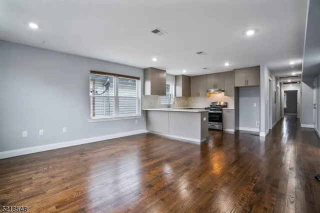 an empty room with wooden floor kitchen view and windows