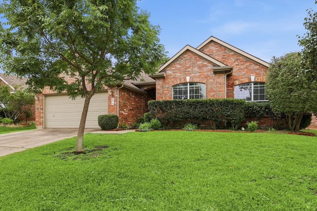 2616 Hollow Ridge Drive Denton, TX 76210 - Photo 3 of 31 Brick facade property featuring an attached garage with a tan door, a concrete driveway, and front landscaping with mature shrubs and trees