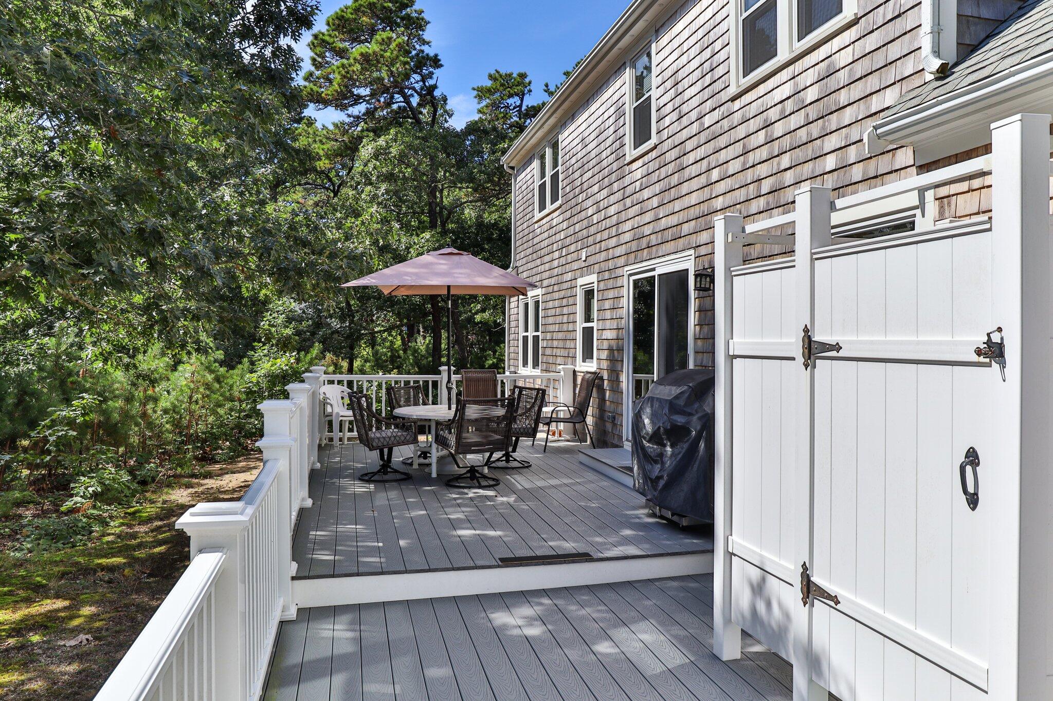 15 Chipmunk Lane Eastham, MA 02642 - Photo 25 of 32 a view of a patio with table and chairs under an umbrella with wooden floor and fence