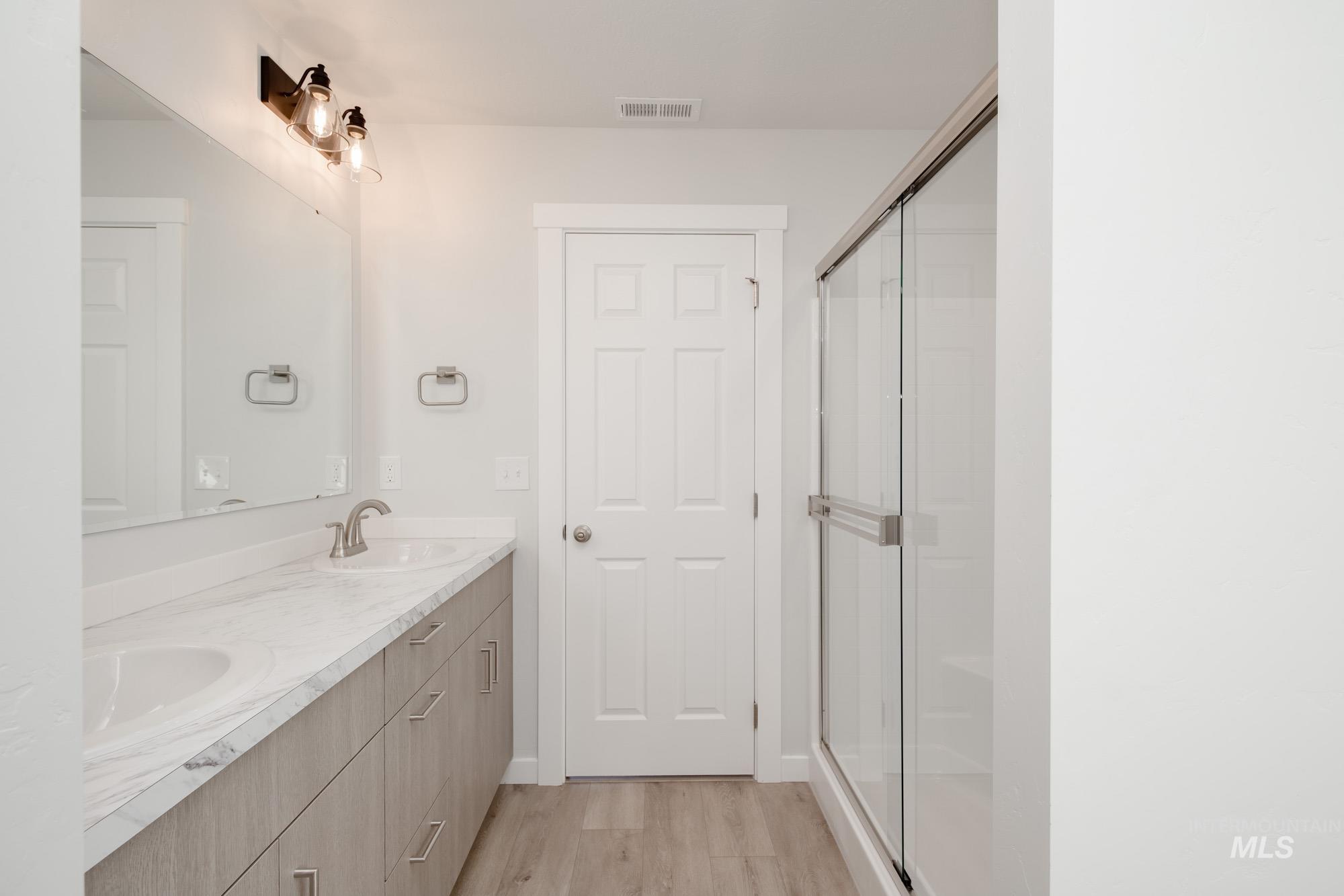 14092 Shiny Spruce Street Caldwell, ID 83607 - Photo 22 of 22 Bathroom featuring a dual vanity with a light wood-finish cabinet and stone-look countertop, undermount sinks, and a framed glass shower enclosure