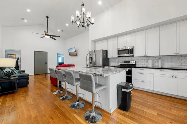 a kitchen with stainless steel appliances kitchen island granite countertop a sink dishwasher a stove top oven a dining table and chairs with wooden floor