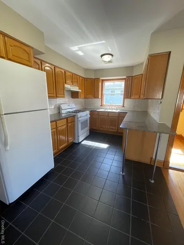 a kitchen with granite countertop a sink a stove a refrigerator a washer dryer and white cabinets