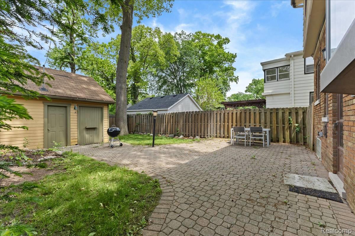 Expansive brick paver patio with a wood privacy fence and a detached accessory structure