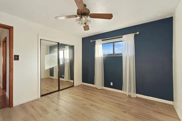 a view of an empty room with wooden floor and a ceiling fan