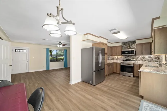 a kitchen with stainless steel appliances granite countertop a refrigerator a sink dishwasher a stove and a dining table with wooden floor