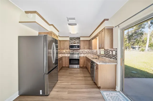 a kitchen with stainless steel appliances granite countertop a refrigerator a sink dishwasher a stove and white countertops with wooden floor