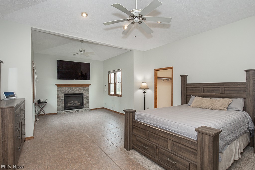 7484 Oberlin Road Elyria, OH 44035 - Photo 10 of 27 Tiled bedroom with a spacious closet, a stone fireplace, ceiling fan, and a textured ceiling