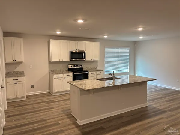 a view of a kitchen with kitchen island a sink wooden floor and stainless steel appliances