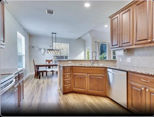 a kitchen with stainless steel appliances granite countertop a sink dishwasher cabinets and dining table with wooden floor