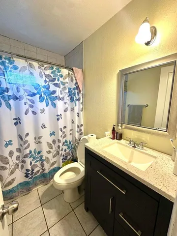 a bathroom with a granite countertop sink a toilet a mirror and shower curtain