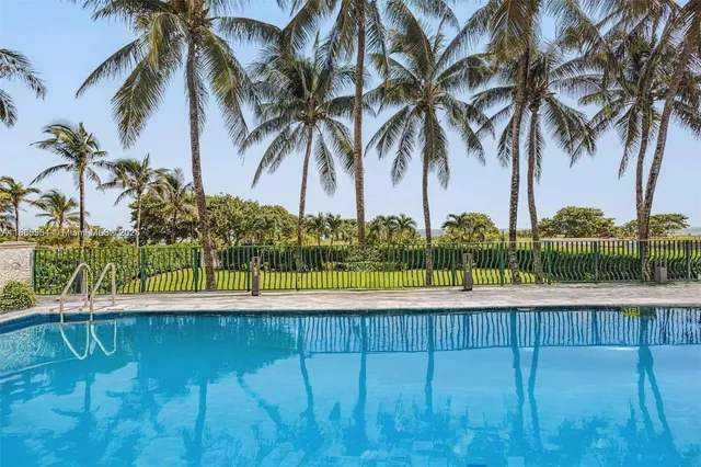 a view of swimming pool with a lawn chairs under palm trees