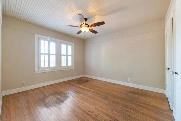 an empty room with wooden floor fan and windows