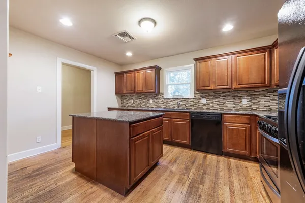 a kitchen with stainless steel appliances granite countertop wooden cabinets a sink and dishwasher a stove with wooden floors