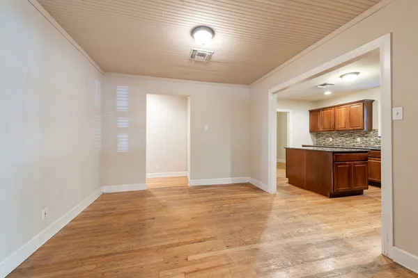 a view of an empty room and a kitchen with wooden floor