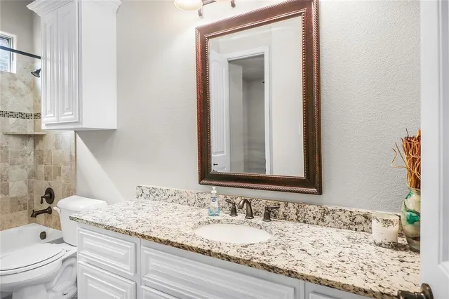 a bathroom with a granite countertop bathtub sink vanity mirror and toilet