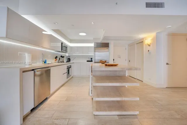 a living room with stainless steel appliances kitchen island granite countertop a refrigerator and a sink