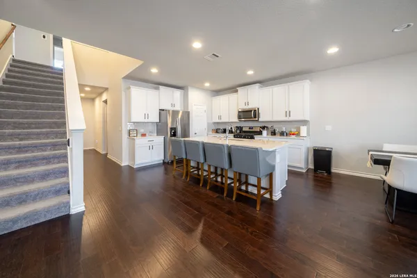 a open kitchen with stainless steel appliances granite countertop a stove top oven a refrigerator a dining table and chairs with wooden floor