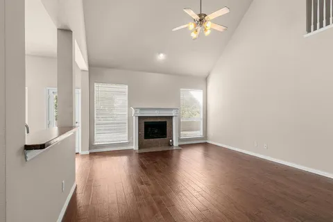 an empty room with wooden floor a ceiling fan a fireplace and windows